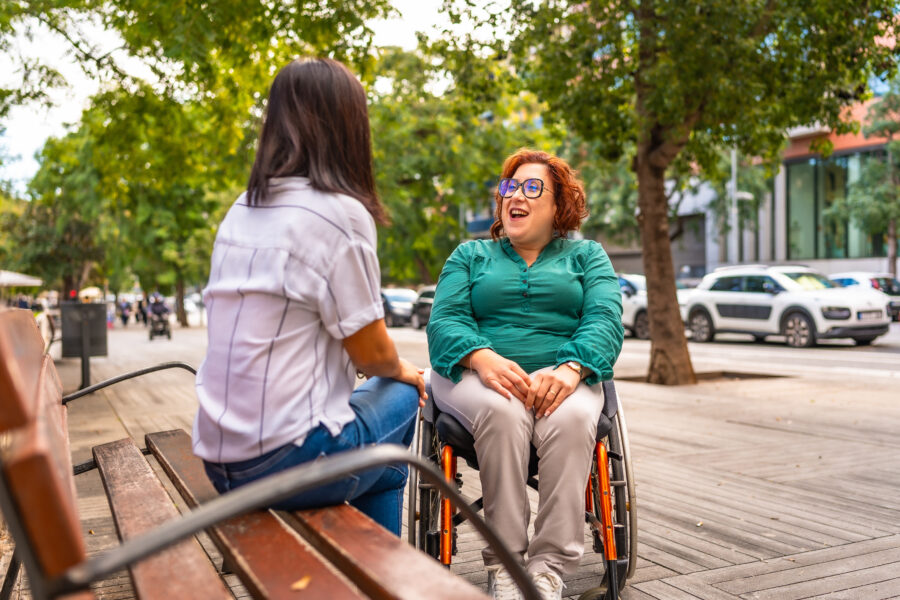 Woman with disability talking with friend sitting on a bench